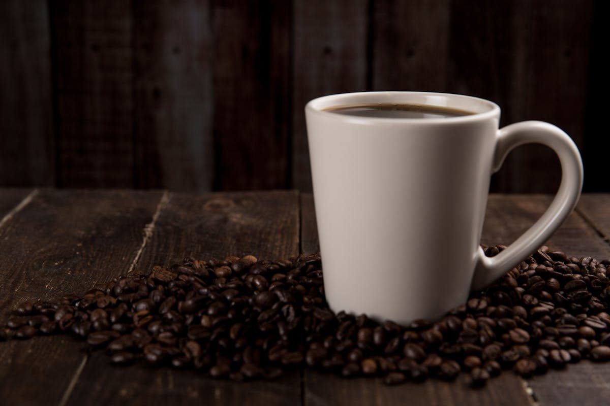 Granos de cafe enteros junto a cafe recien molido en un molinillo